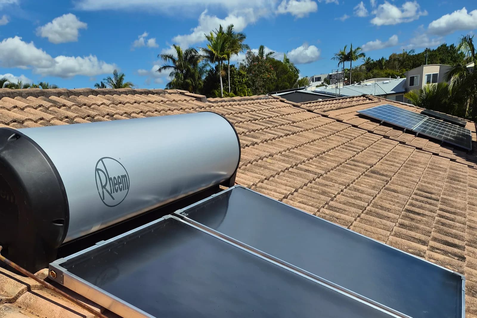A rooftop solar hot water installation by RCM, with Sunshine Coast houses and palms behind